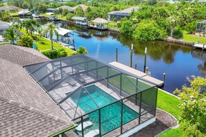 A rooftop pool with a glass enclosure, surrounded by lush greenery and a calm water body. - Serene Living in Port Charlotte, 5937 (Charlotte County)