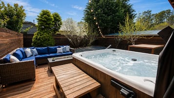 A wooden deck with a hot tub, a blue sofa, and a wooden table.