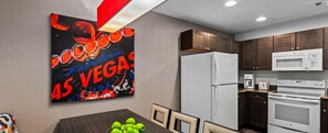 A kitchen with a refrigerator, microwave, and oven. There is a table with a bowl of fruit and a wall-mounted artwork. - Club Wyndham Tropicana 2 Bedroom Suite (Las Vegas)