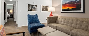 A hotel room with a blue armchair, a beige sofa, a framed picture of a sunset, and a lamp. - Club Wyndham Tropicana 2 Bedroom Suite (Las Vegas)
