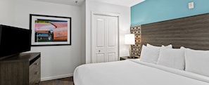 A hotel room with a bed, a TV, a door, and a wall-mounted lamp. - Club Wyndham Tropicana 2 Bedroom Suite (Las Vegas)