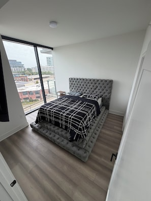 A bedroom with a large bed, a tufted headboard, and a view of buildings through a large window. - Midtown Atlanta 2 bedroom luxury condo (Atlanta)