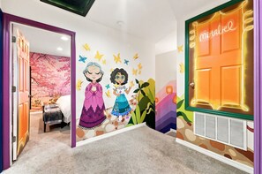 Ein Kinderzimmer mit Wandgemälde, einem Bett, einer Tür mit der Aufschrift 'Wunder' und einer Heizung.