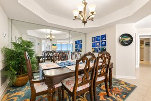 A dining area with a large mirror, wooden chairs, a chandelier, and a potted plant. - Oceanfront Maisons Sur Mer | Amazing Ocean Views (Myrtle Beach)
