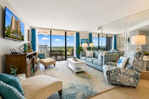 A spacious living room with a balcony, a sofa set, a coffee table, and a TV mounted on the wall. - Oceanfront Maisons Sur Mer | Amazing Ocean Views (Myrtle Beach)