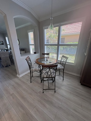A dining area with a round table and four chairs, a hanging light fixture, and large windows with blinds. - Luxury pool home in the Venetian Golf and River Club (North Venice)