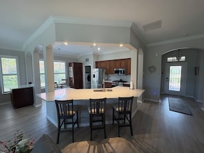 A spacious kitchen with a central island, wooden cabinets, and a dining area with chairs. - Luxury pool home in the Venetian Golf and River Club (North Venice)
