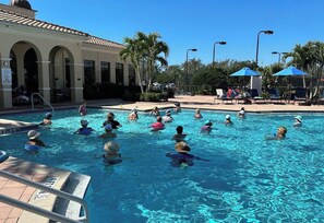 A swimming pool with people in the water, a building with arches, and palm trees in the background. - Luxury pool home in the Venetian Golf and River Club (North Venice)