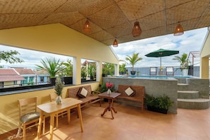 Una terraza con piscina, muebles de madera y plantas en macetas.
