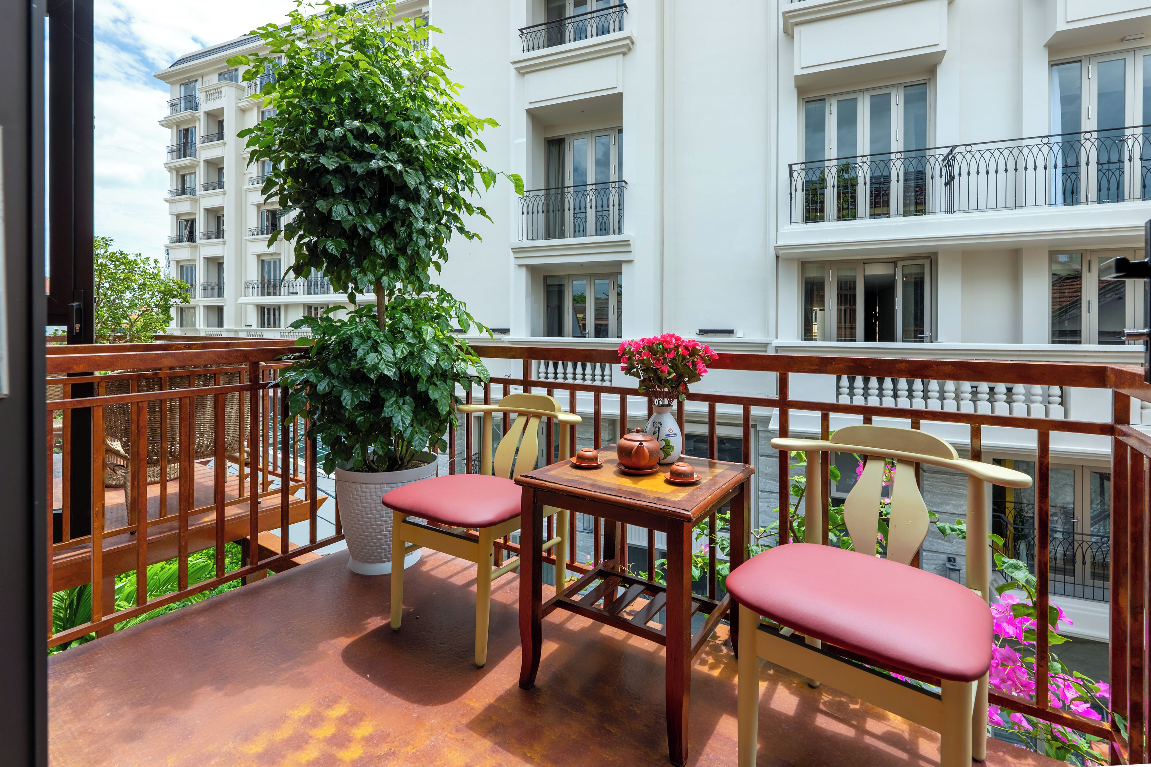 Een balkon met een houten tafel, twee stoelen, een bloempot en een vaas met bloemen.