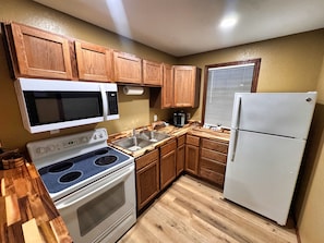 A kitchen with wooden cabinets, a microwave, a stove, a sink, and a refrigerator.