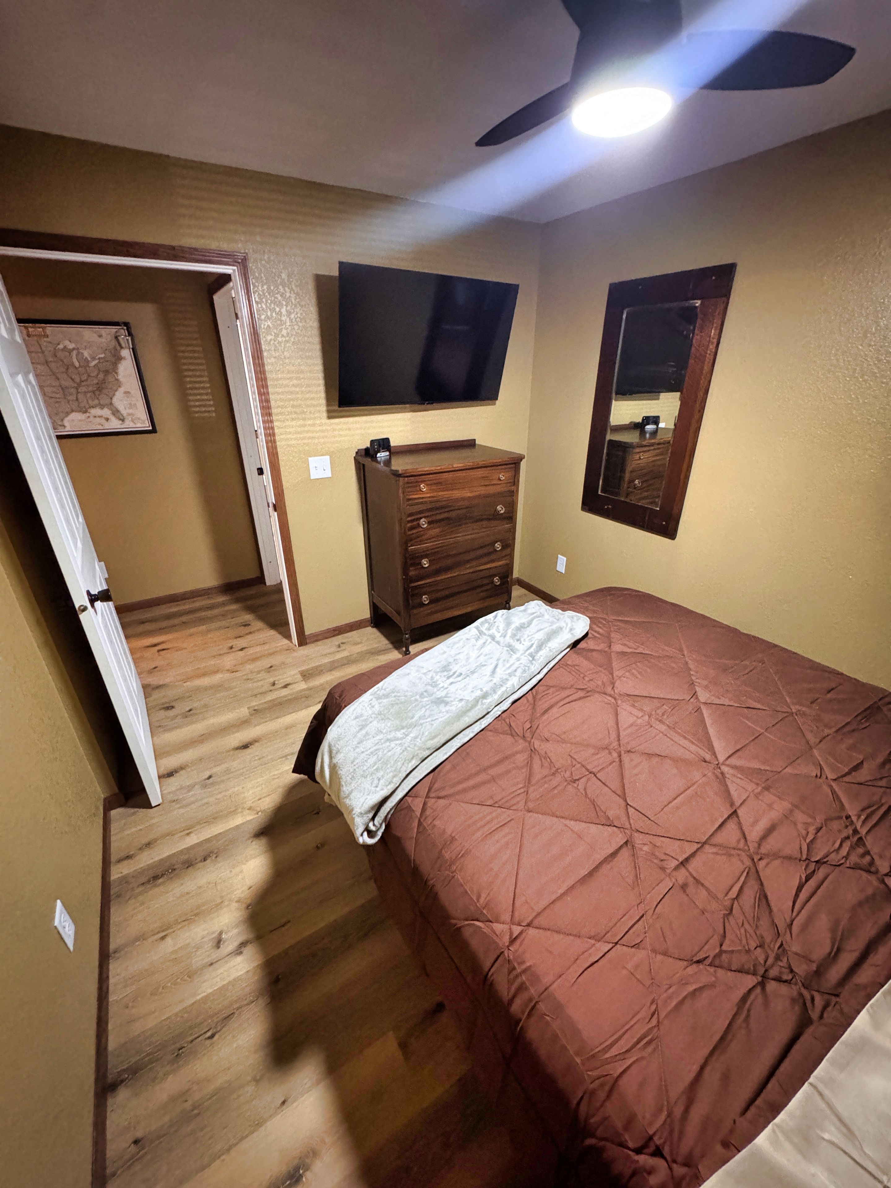 A bedroom with a bed, dresser, television, and a ceiling fan.