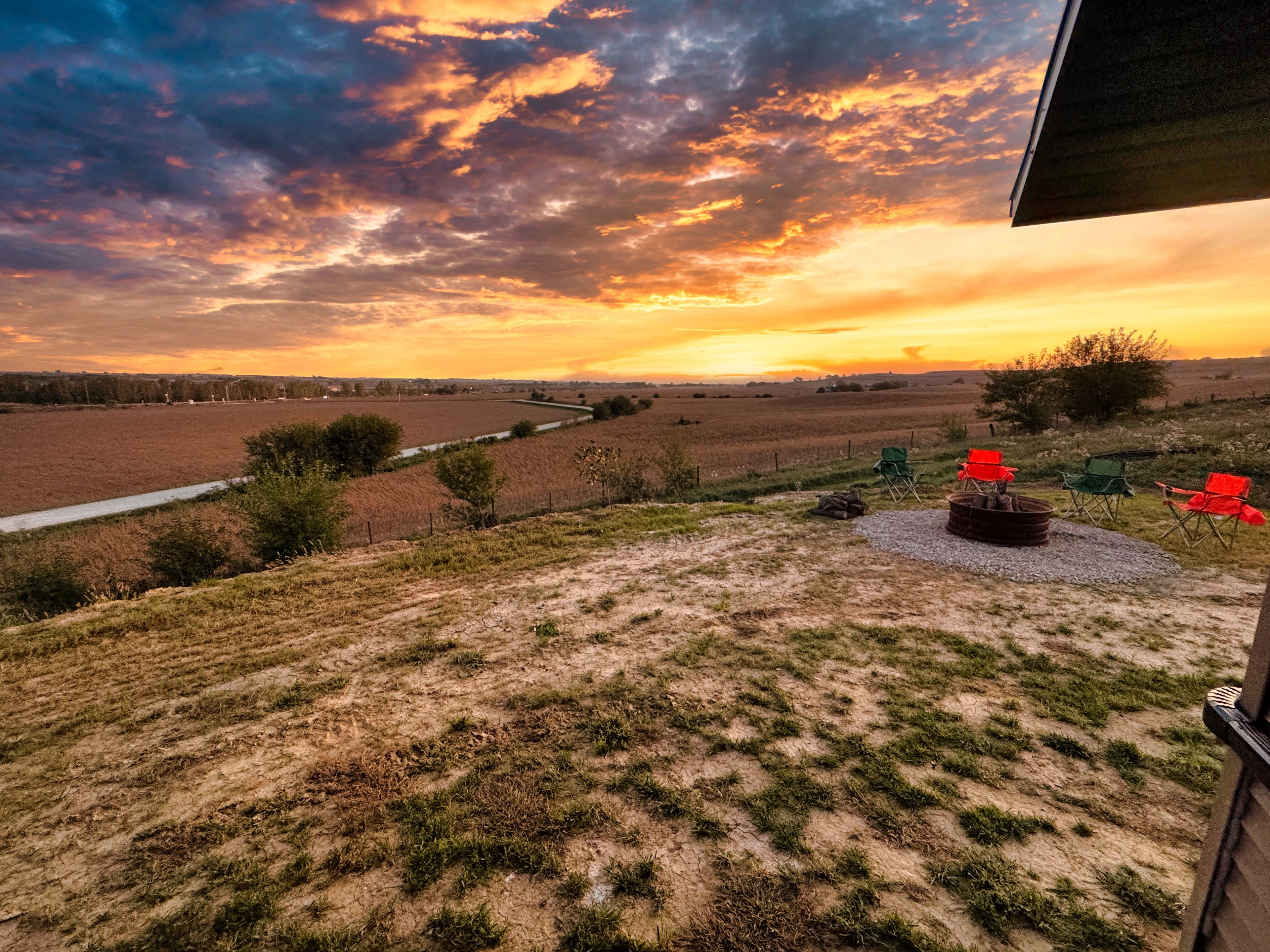 A rural landscape with a sunset, open fields, a dirt path, and outdoor seating.