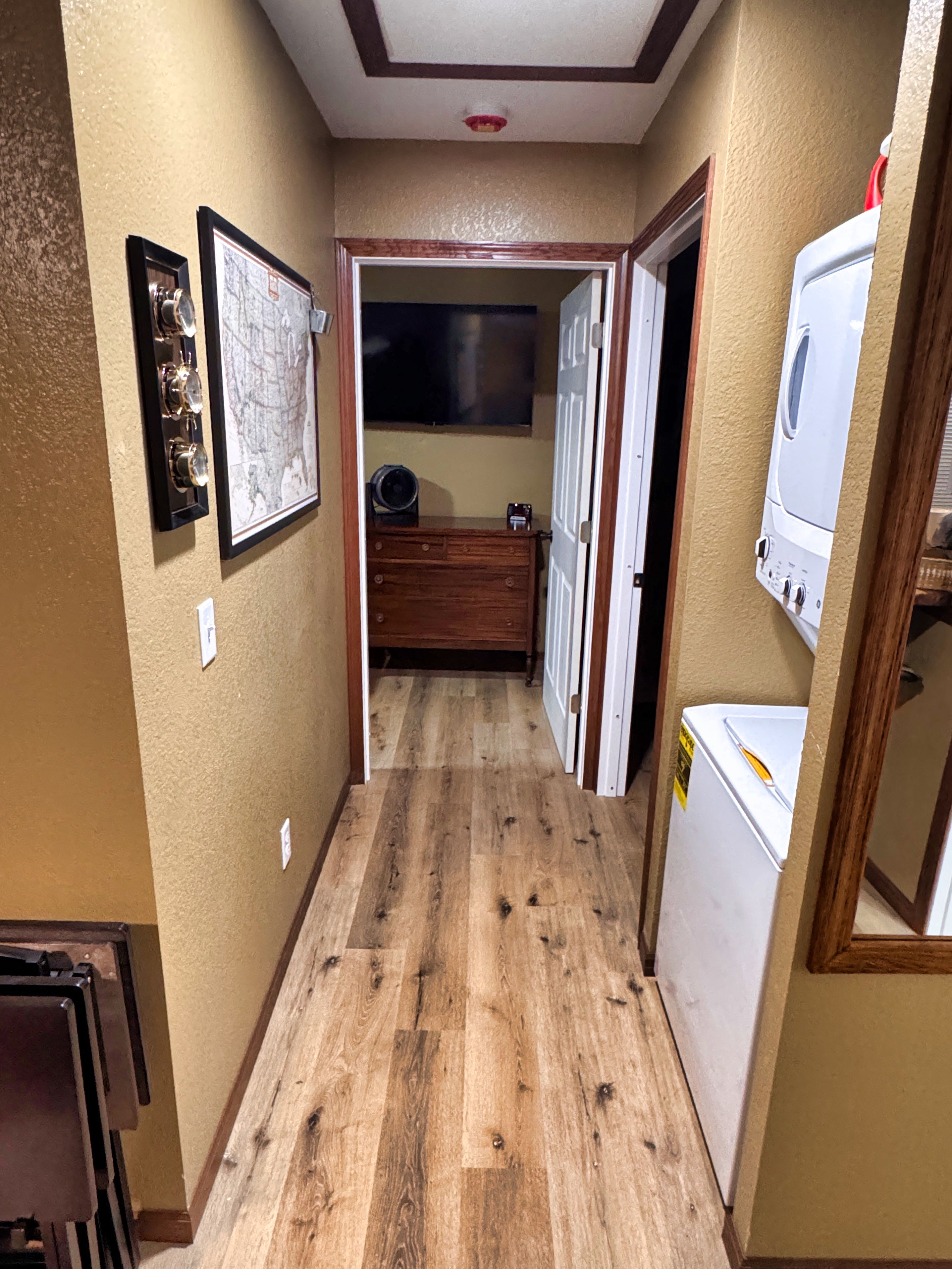 A narrow hallway with wooden flooring, a wooden dresser, a white washing machine, and a framed map on the wall.
