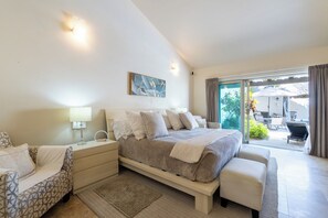 Une chambre moderne avec un grand lit, des tables de chevet, un canapé et une vue sur l’espace extérieur grâce à une porte-fenêtre coulissante.