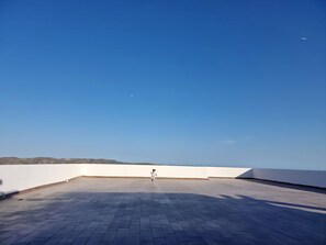 Eine Dachterrasse mit blauem Himmel, einem gepflasterten Boden und weiter Aussicht auf eine Landschaft.