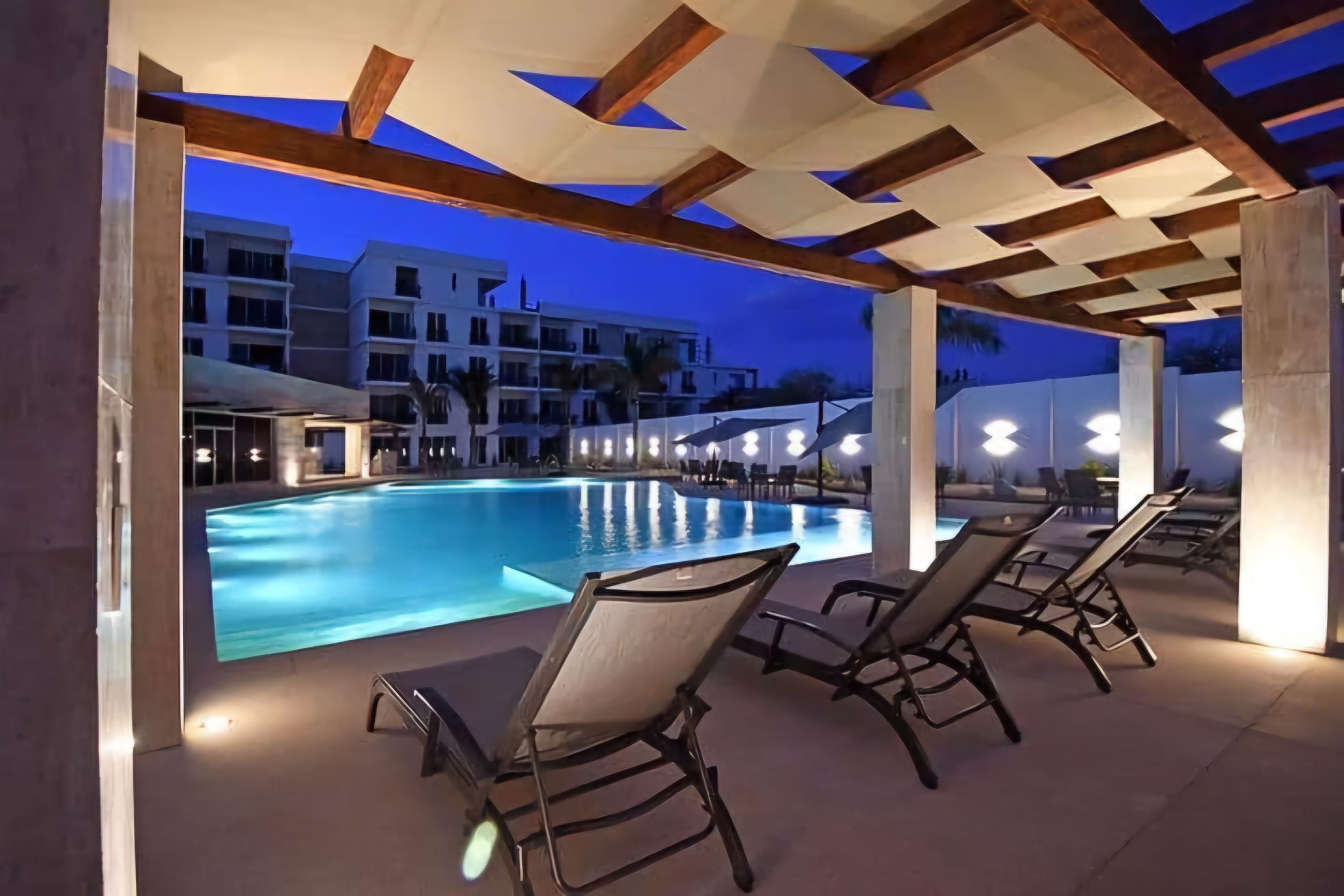 Un espace piscine extérieur avec des chaises longues et une vue sur un immeuble à plusieurs étages en arrière-plan.