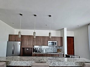 Eine moderne Küche mit einem Edelstahl-Kühlschrank, einer Mikrowelle und einem eingebauten Backofen. Holzschränke und eine Granit-Arbeitsplatte ergänzen das Bild.