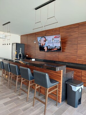 A modern kitchen with a wooden countertop, bar stools, a trash bin, and a TV screen displaying a live event. - Spacious 3-bedroom Penthouse,with a beautiful view in fabulous San José del Cabo (San José del Cabo)
