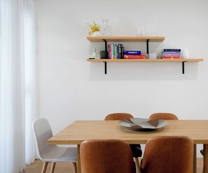 A dining area with a wooden table, two chairs, and a bookshelf above. - Wooloowin Escape Modern Comfort and Sunlit Courtyard (Brisbane)