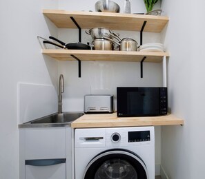 A compact kitchen with a washing machine, a toaster, and a microwave on a wooden shelf. - Wooloowin Escape Modern Comfort and Sunlit Courtyard (Brisbane)