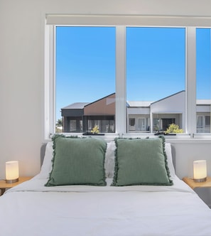 Ein Schlafzimmer mit einem großen Fenster, zwei grünen Kissen und Nachttischlampen.