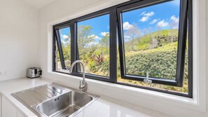 A kitchen with a stainless steel sink, a toaster, and a window overlooking a green landscape.