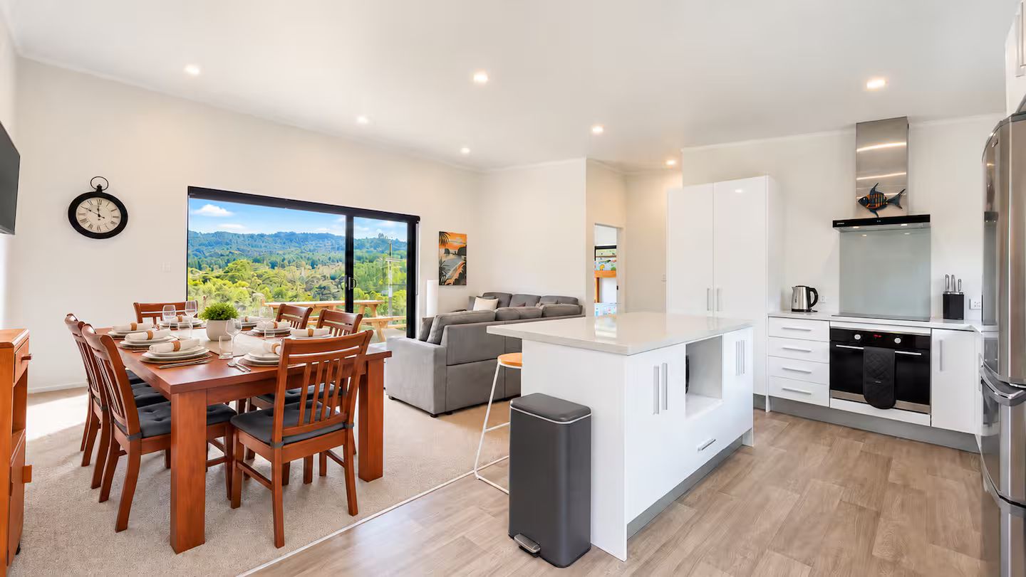 A modern kitchen with white cabinets, a built-in oven, and a large window offering a view of greenery.