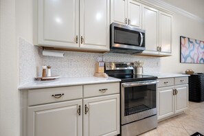 A kitchen with white cabinetry, a stainless steel microwave, a stove, and an oven. - Relaxing pool home at Sarasota National Peace In The Palms (Venice)