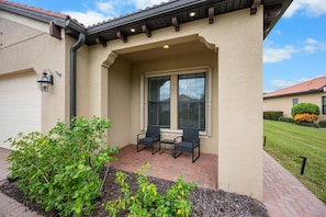 A house with a covered patio, two chairs, and a table. - Relaxing pool home at Sarasota National Peace In The Palms (Venice)