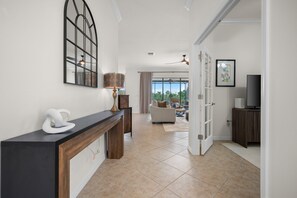 A modern living room with a sofa, a TV, and a dining area with a table and chairs. - Relaxing pool home at Sarasota National Peace In The Palms (Venice)