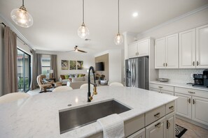 A modern kitchen with a central island, stainless steel appliances, and pendant lighting. - Relaxing pool home at Sarasota National Peace In The Palms (Venice)