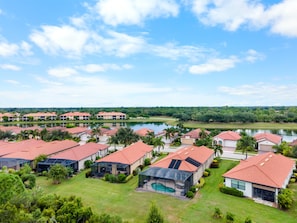 A residential area with multiple houses, a swimming pool, and a lake in the background. - Relaxing pool home at Sarasota National Peace In The Palms (Venice)