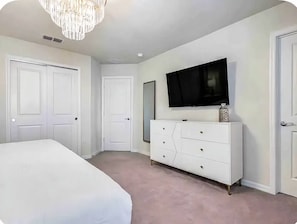Une chambre à coucher avec un lit, une commode, un téléviseur et deux portes.