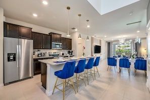 A modern kitchen with a stainless steel refrigerator, a microwave, and a built-in oven. There are blue bar stools and a dining table with chairs. - 6BR Pool Home Near Disney at Windsor Island (Davenport)