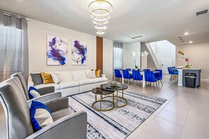 Un salon moderne avec un canapé, une table basse et un coin repas avec des chaises bleues.