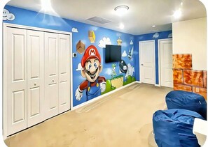 A room with a Mario mural, white doors, a flat-screen TV, and a blue couch. - 5BR Disney-Themed Getaway with Pool (Davenport)