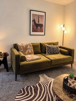 A living room with a green sofa, a framed picture on the wall, a floor lamp, a small table with a plant, and a zebra-patterned rug. - Spacious 5BR Durham Home | Ideal for Contractors (Bearpark)