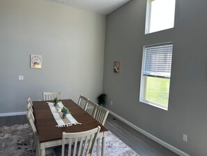 Un comedor con una mesa de madera, sillas blancas, un camino de mesa de encaje y una pequeña planta en maceta.