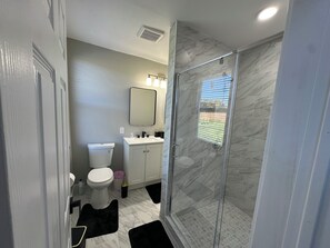 Un baño con inodoro, lavabo, espejo y zona de ducha con mampara de vidrio.
