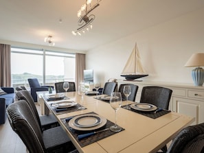 Ein Hotel-Esszimmer mit einem langen Tisch, gedeckt für sechs Personen, umgeben von Korbstühlen, einer Segelboot-Dekoration und einem Fernseher an der Wand.