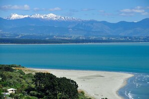 A coastal landscape with a beach, a mountain range, and a clear sky. - Moana View - Elevated Beachside Home with Panoramic Ocean Views (Nelson)