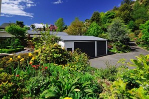 A residential area with a garage, lush greenery, and a clear sky. - Moana View - Elevated Beachside Home with Panoramic Ocean Views (Nelson)
