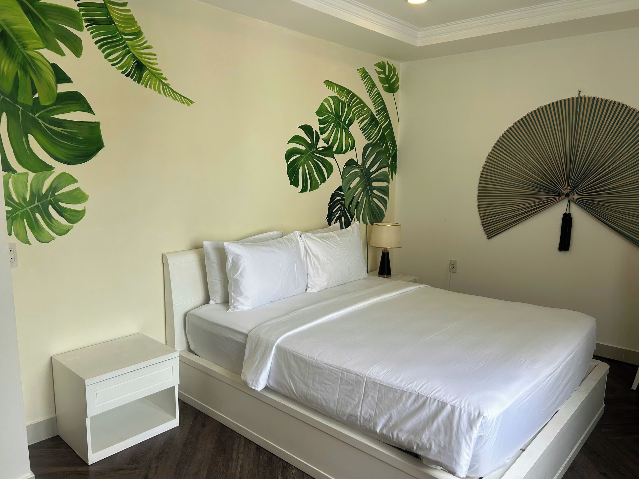 A bed with white bedding, a bedside table, a lamp, and a wall-mounted fan.