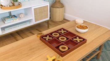 Una mesa de madera con un juego de tres en raya, un tazón de cereal y una estantería con libros y objetos decorativos.