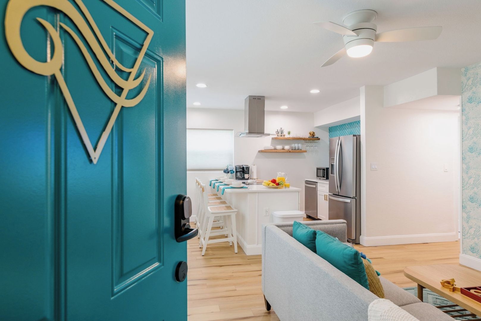 A modern kitchen with a teal door, white cabinetry, and a central island with fruit.