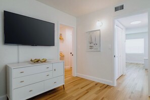 Un saló modern amb un televisió de pantalla plana, un llum blanc i un dibuix arquitectònic emmarcat a la paret.