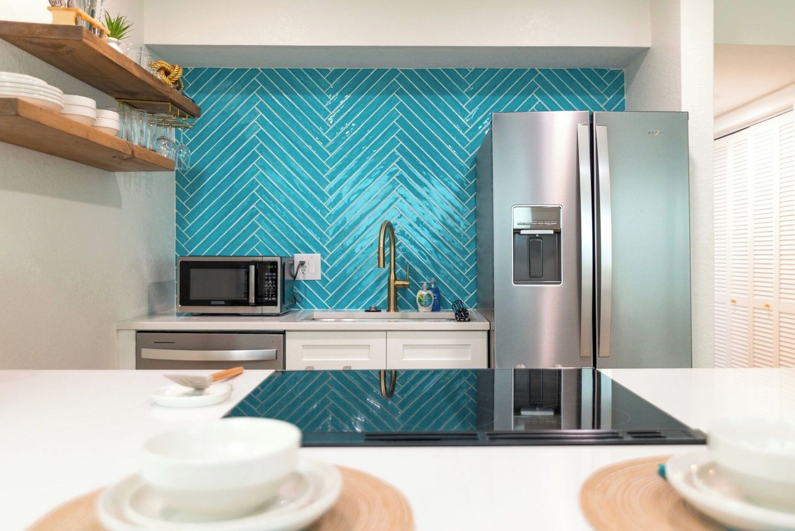 A modern kitchen with a herringbone tile backsplash, stainless steel appliances, and a black countertop.