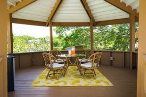 Un espacio al aire libre cubierto con una mesa y cuatro sillas, un tapete amarillo estampado y vistas a la vegetación.