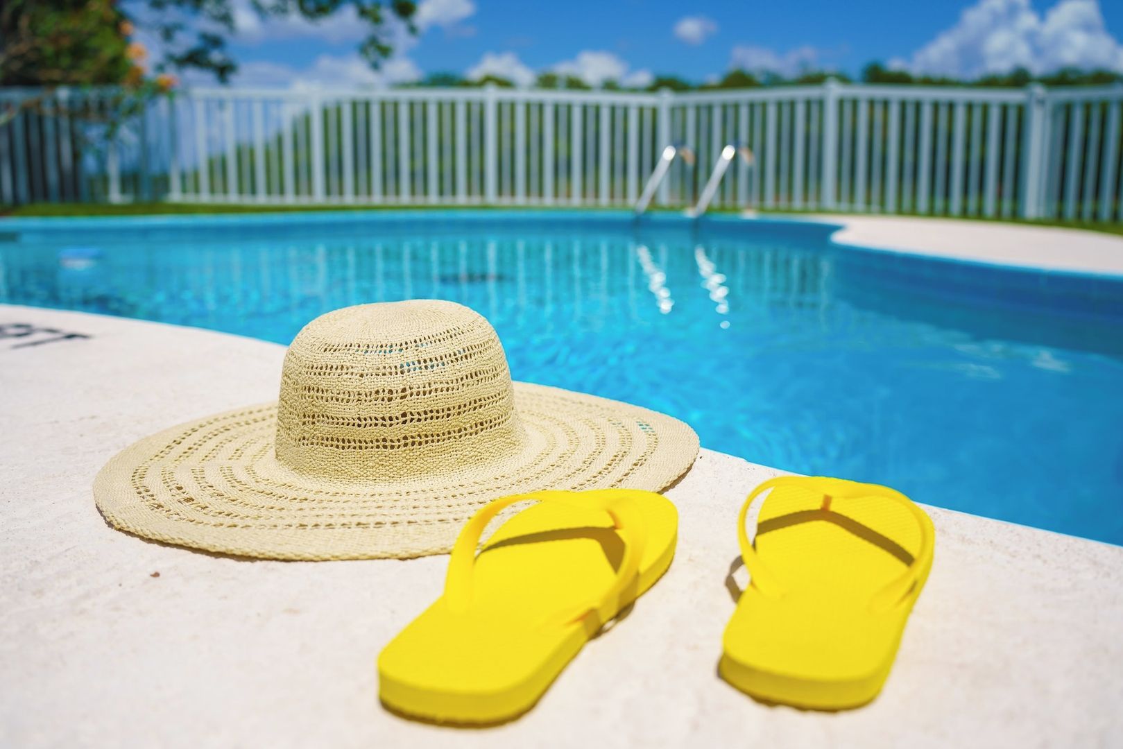 A poolside setting with a hat and yellow flip-flops on a white surface.